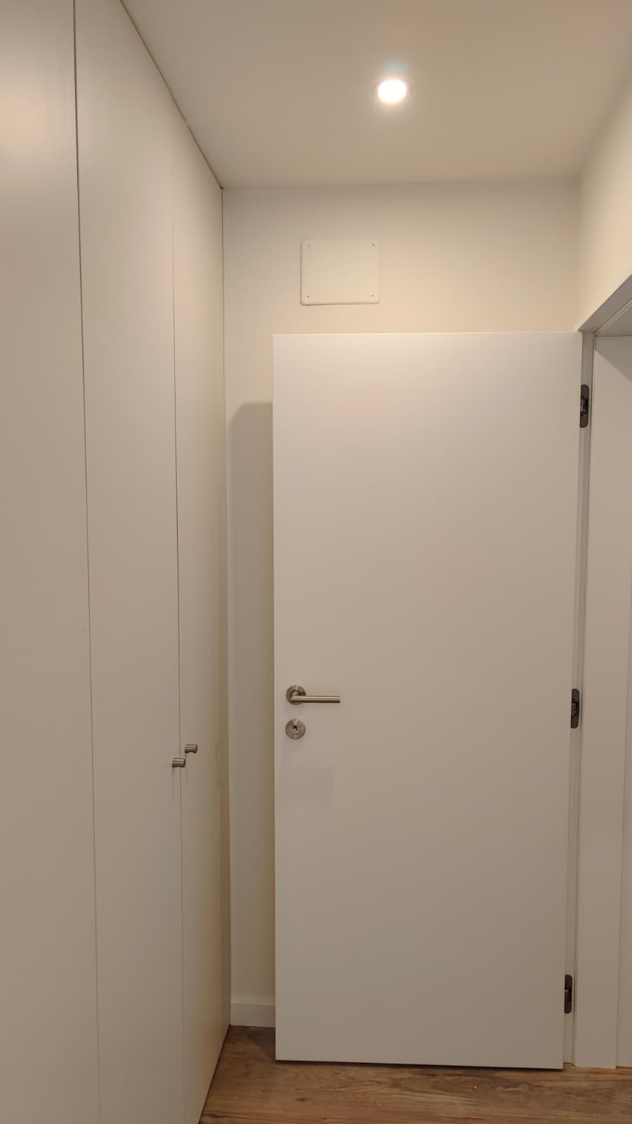 Porta de interior branca de núcleo denso, com puxador em inox, ao lado de um roupeiro embutido